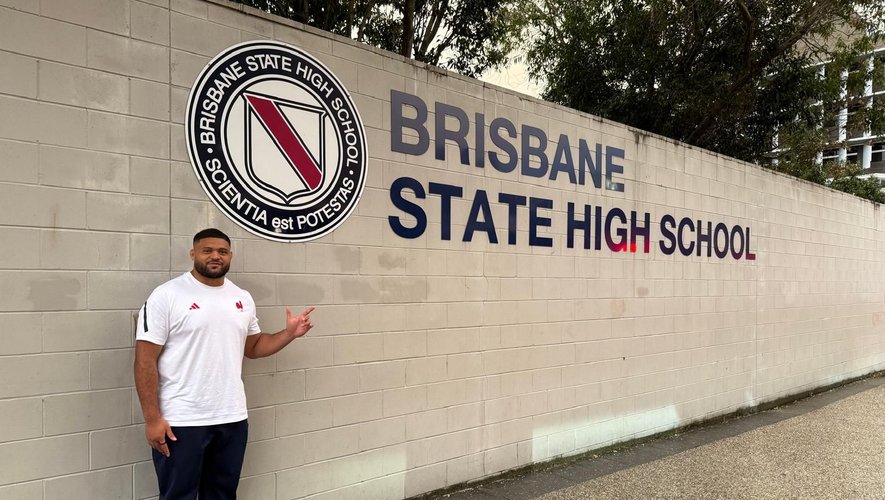 Moses Alo-Emile devant son ancien lycée à Brisbane dont la devise en latin signifie La science est le pouvoir.